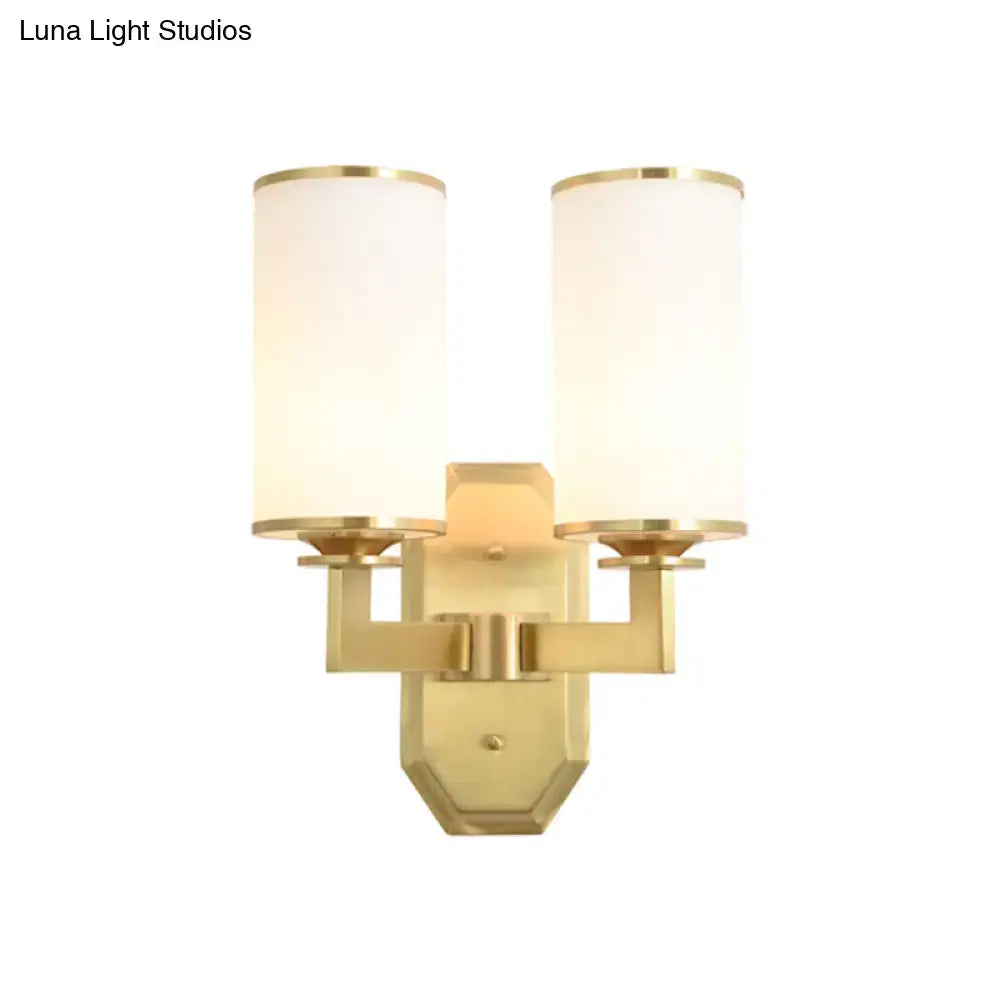 Modern gold wall sconce with two cylindrical opal glass shades and white fabric covers for bedroom lighting