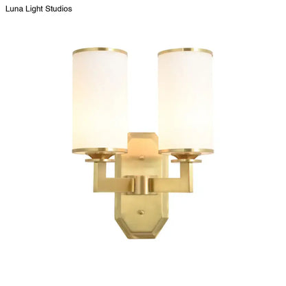 Modern gold wall sconce with two cylindrical opal glass shades and white fabric covers for bedroom lighting