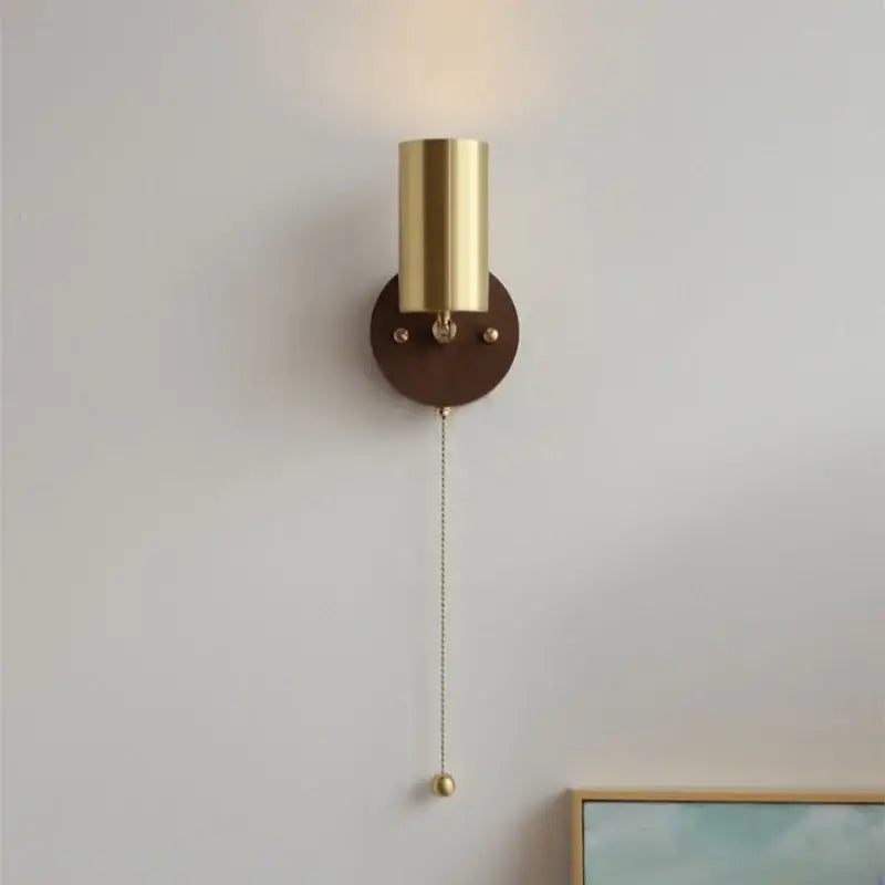 Modern gold cylindrical wall sconce with dark brown walnut leather base and pull chain switch for bedroom lighting