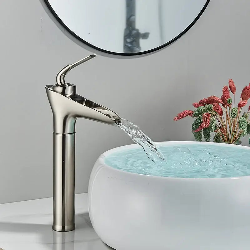 Modern gold waterfall wine glass basin faucet in brushed nickel with sleek tall design flowing into ceramic vessel sink