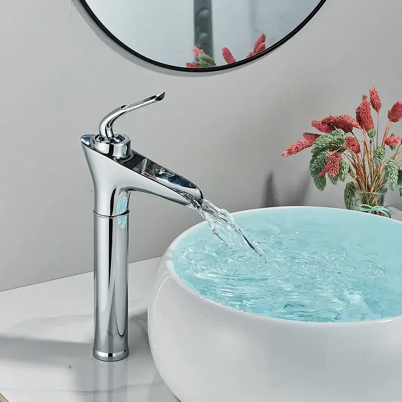 Modern gold waterfall wine glass basin faucet with chrome finish and sleek design flowing water into white ceramic sink