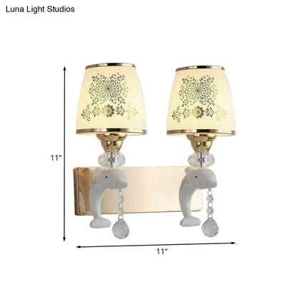 A pair of modern gold and white dolphin wall sconces with opal glass shade and crystal teardrop accents for bedroom use
