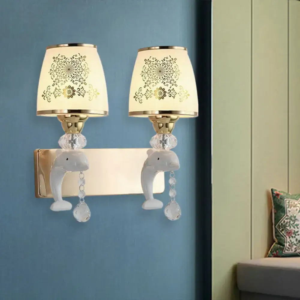 A pair of modern gold and white dolphin wall sconces with cream opal glass shade and crystal droplets for bedroom use