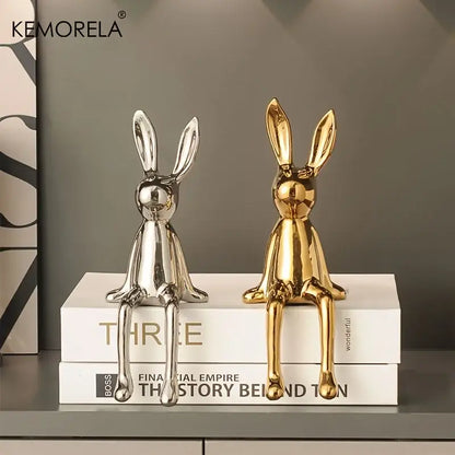 Two glossy ceramic sitting rabbit ornaments in silver and gold on stacked books for modern living room decor