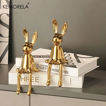 Two glossy gold ceramic sitting rabbit ornaments in varying sizes displayed on stacked books for living room decor