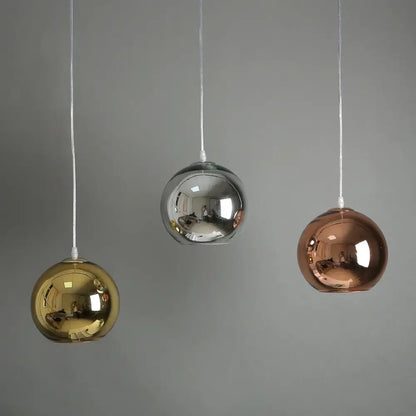Three spherical decorbites golden ball glass pendant lights in gold silver and rose gold hang against a gray background