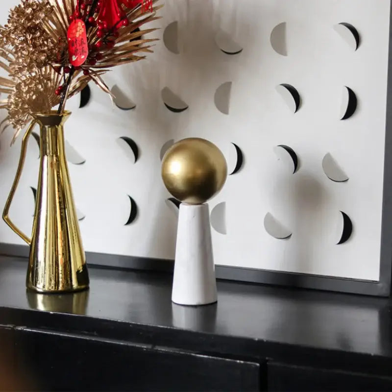 A sleek modern golden ball marble cone sculpture with a polished gold sphere on a white marble pedestal for living room decor