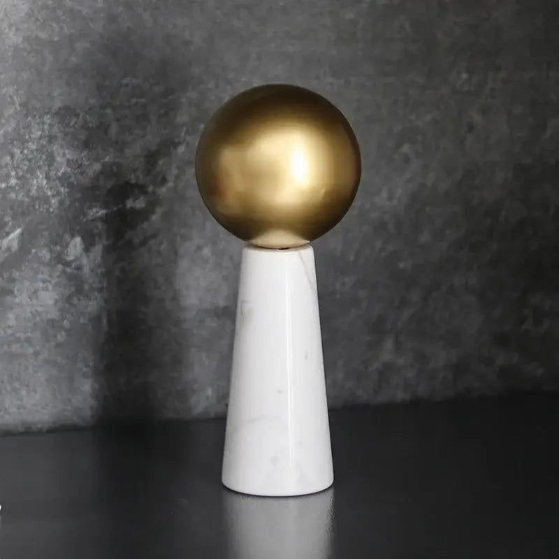 A modern golden ball spherical ornament on a white marble cone pedestal for stylish living room decor