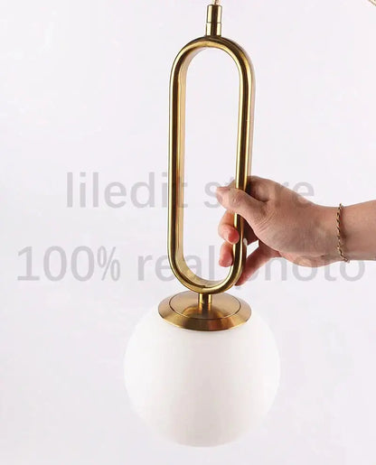 Modern golden glass ball pendant light with sleek oval metal frame and white spherical glass shade by decorbites
