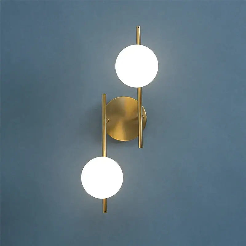 Modern gold-toned decorbites golden indoor wall sconce with two spherical frosted glass shades for bedroom use