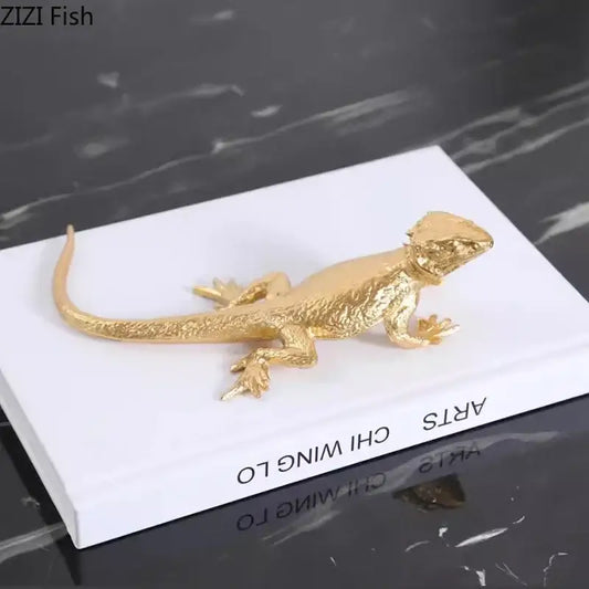 Modern golden lizard sculpture metal desk ornament with textured scales resting atop a white book