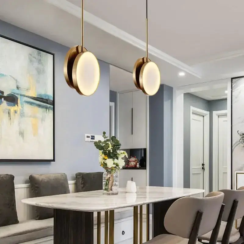 Two modern pendant lights with golden marble led shades and gold-toned frames hang above a dining table decorbites golden marble