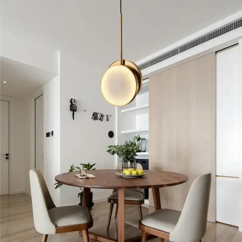 A modern pendant light with a warm glowing circular shade and slender brass rod from decorbites golden marble led collection