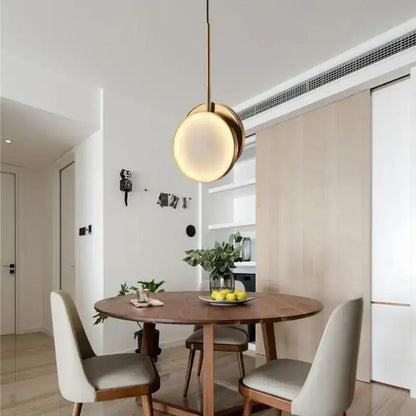 A modern pendant light with a warm glowing circular shade and slender brass rod from decorbites golden marble led collection