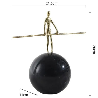 A slender gold-toned golden metal abstract figure sculpture balancing on a polished black marble sphere for living room decor