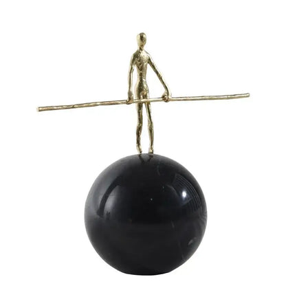 A slender golden metal abstract figure sculpture holding a rod on a black spherical base for living room decorbites decor
