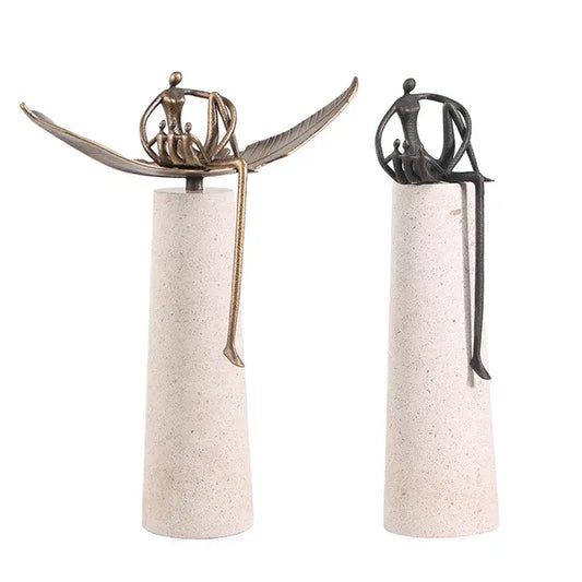 Two golden metal abstract figure sculptures seated on leaf forms atop textured concrete pedestals for living room decorbites decor