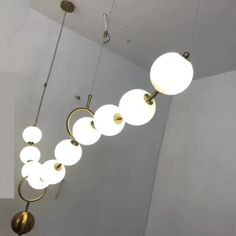 A modern golden necklace chandelier with frosted white glass globes and gold-toned metal rings for dining room luxury