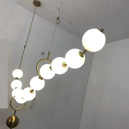 A modern golden necklace chandelier with frosted white glass globes and gold-toned metal rings for dining room luxury