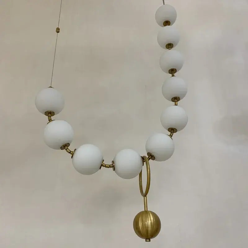 A modern golden necklace chandelier featuring matte white beads and a textured gold sphere for luxury dining room lighting