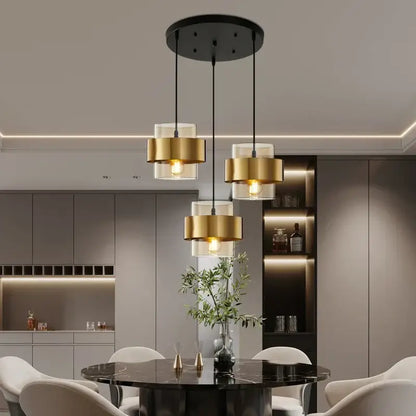 Modern golden pendant lights featuring three gold-finished cylindrical shades and clear glass diffusers hanging from a black mount
