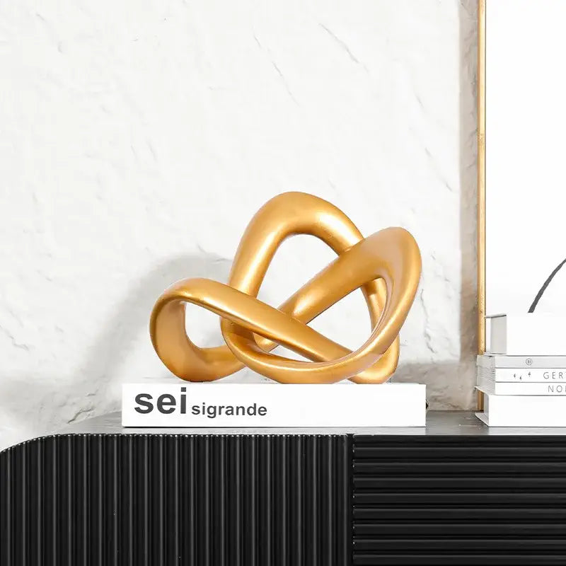 Modern golden twisted dough rope knot sculpture resting on a white book for living room decor
