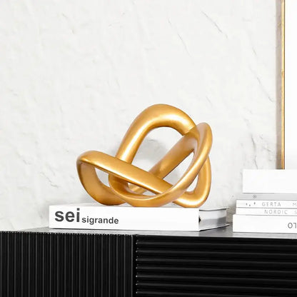 Modern golden twisted dough rope knot sculpture with metallic intertwined loops resting on a stack of books