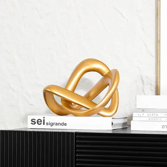 Modern golden twisted dough rope knot sculpture with metallic intertwined loops resting on a stack of books