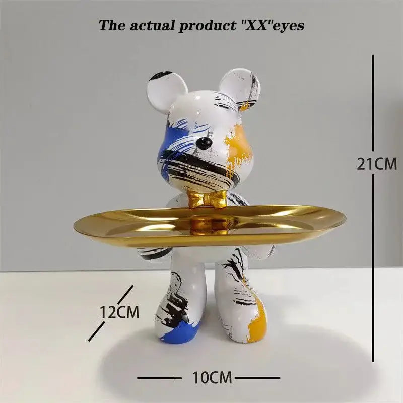 A white bear statue ornament with blue black and yellow paint splatters holds a gold tray for home decor