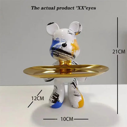 A white bear statue ornament with blue black and yellow paint splatters holds a gold tray for home decor