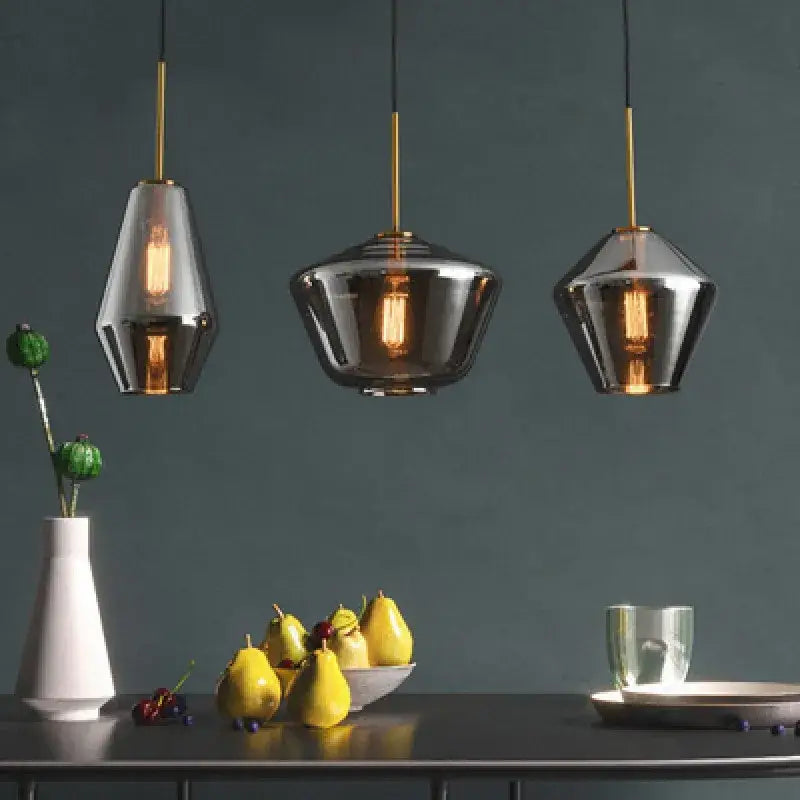 Three modern pendant lamps with gray amber glass shades and gold fixtures illuminate a dining room by decorbites gray amber