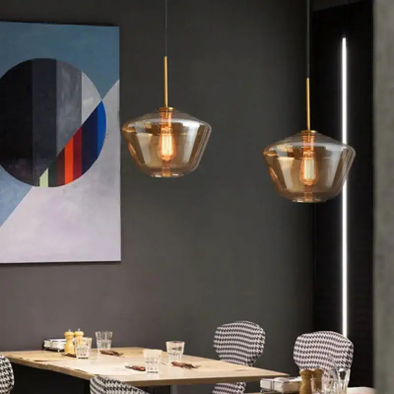 Two amber-tinted gray amber glass pendant lamps with brass rods hang above a dining table decorbites gray amber lighting