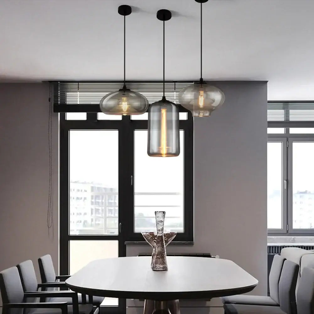 Three modern gray glass pendant lights with smoked glass shades hang above a dining table in a dining room setting
