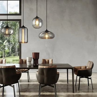 Three modern gray glass pendant lights with frosted and clear finishes hang above a dining table