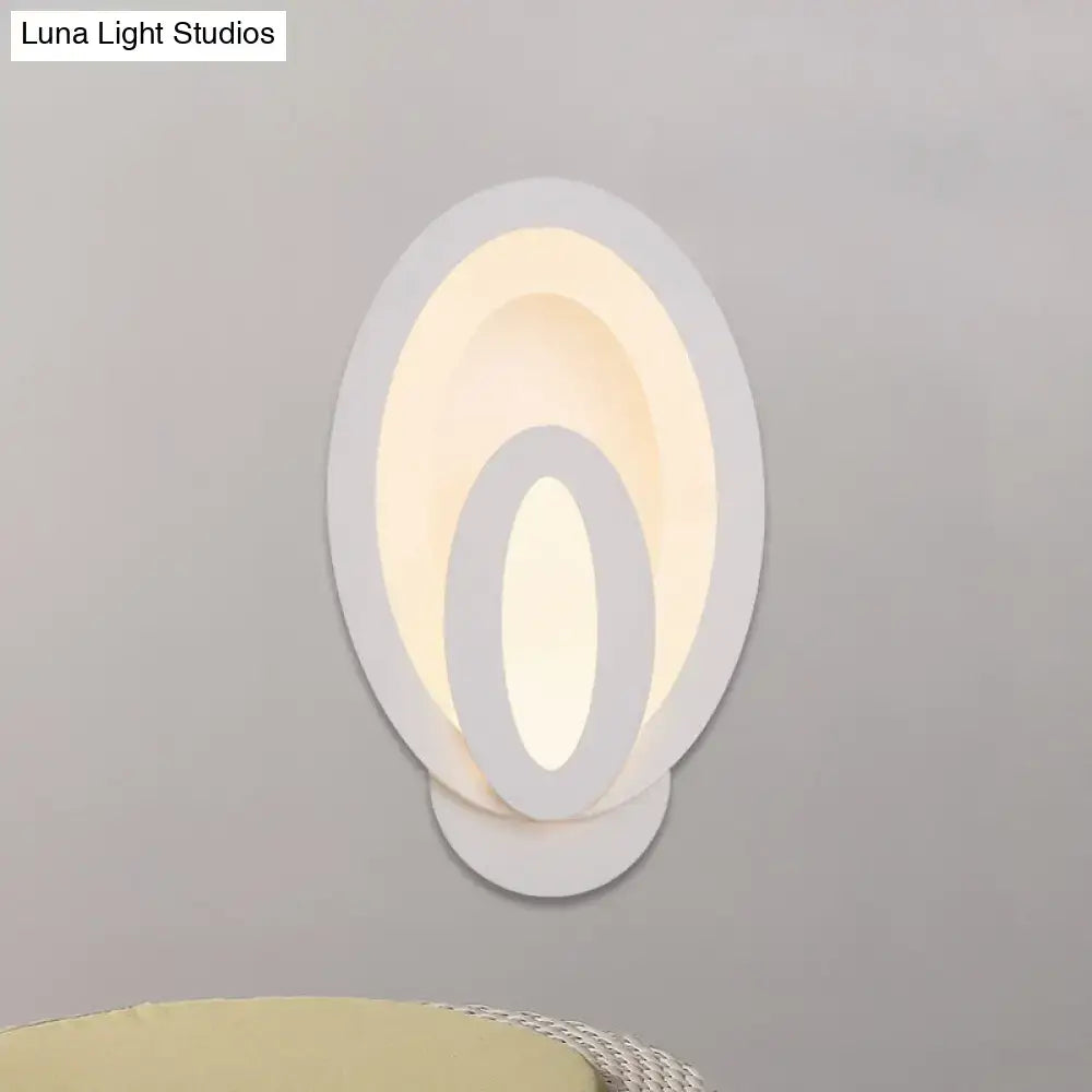 Modern white oval wall sconce with layered concentric rings emits warm white glow with direct wired electric and max bulb wattage