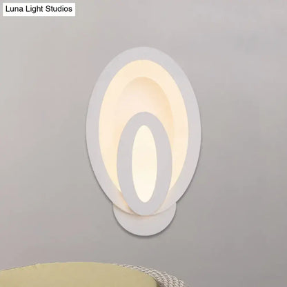 Modern white oval wall sconce with layered concentric rings emits warm white glow with direct wired electric and max bulb wattage