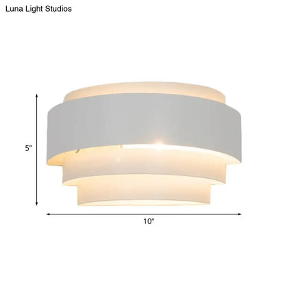 Modern gray metal wall sconce with tiered matte white fabric shades emitting warm glow for living room lighting