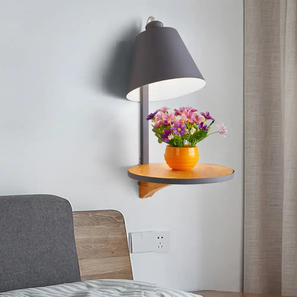 Modern gray tapered shade wall sconce with matte gray conical shade and wooden shelf holding colorful flowers