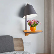 Modern gray tapered shade wall sconce with matte gray conical shade and wooden shelf holding colorful flowers
