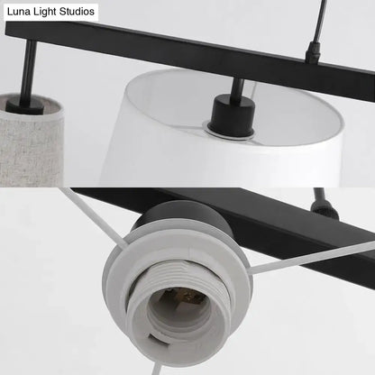 Black metal barrel hanging light fixture with five white fabric lamp shades and visible light bulb sockets