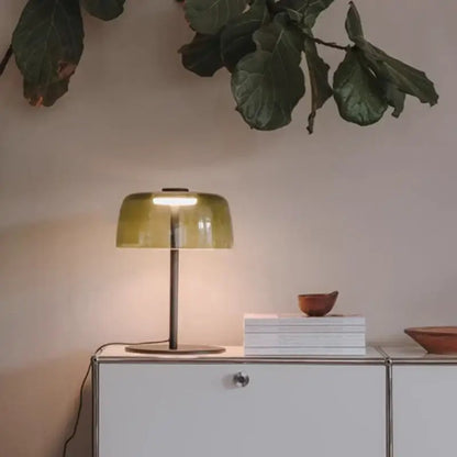 A sleek modern green glass table lamp with an olive-green translucent shade and slender metallic base for bedroom use