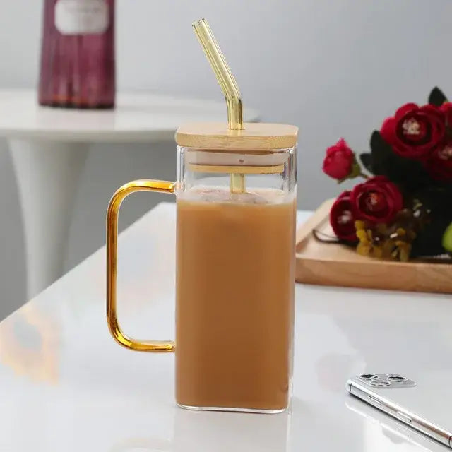 A clear square glass mug with a gold handle and bamboo lid filled with iced coffee for kitchen use