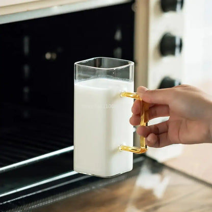 A clear square glass mug with a gold metal handle filled with milk for modern kitchen drinking use