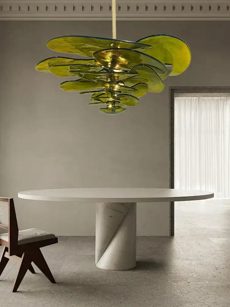 A modern green leaf glass chandelier with layered translucent petals hanging above a white marble dining table