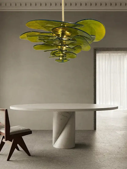 A modern green leaf glass chandelier with layered translucent petals hanging above a white marble dining table