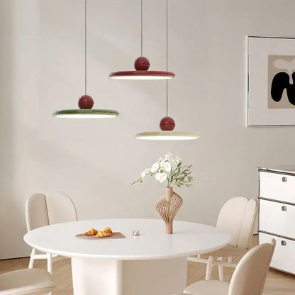 Three modern pendant lights with glossy red tops and cream wind saucer shades hang above a white dining table