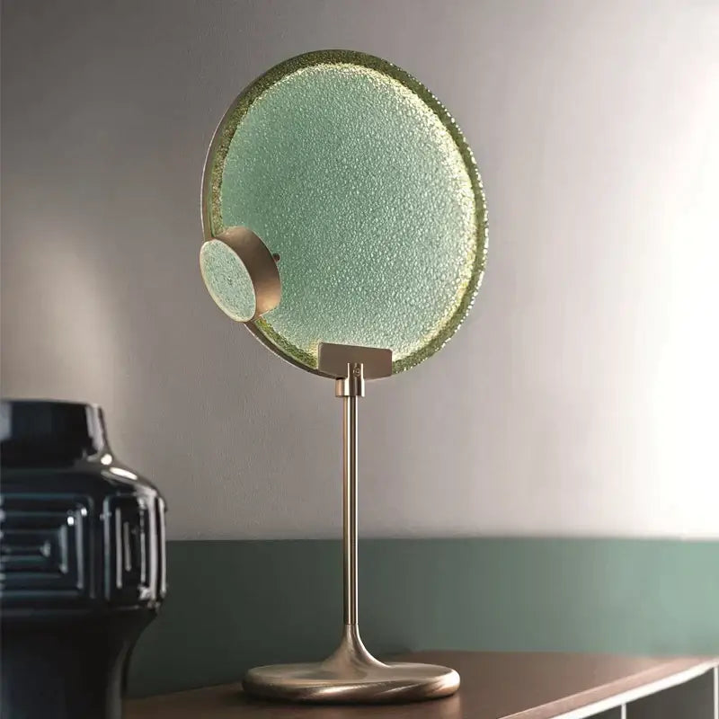 A sleek circular vanity mirror with textured mint green glass and brushed brass frame matching decorbites brass pendant light