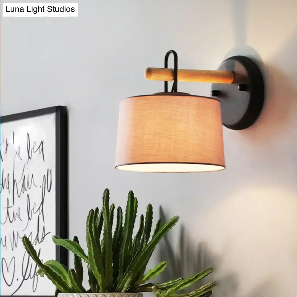Modern grey drum shade wall lamp with warm-toned fabric drum shade mounted on black metal lighting fixture with wood arm