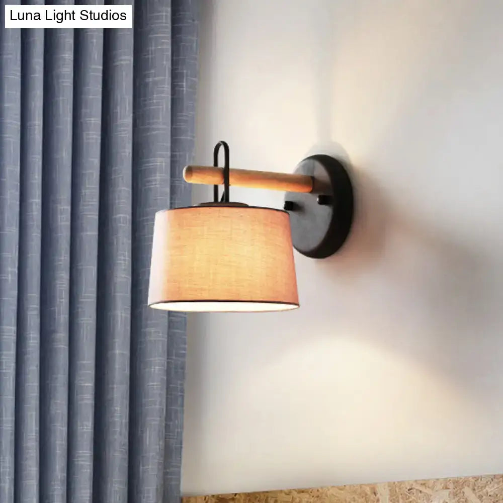 Modern grey drum shade wall lamp with warm-toned fabric shade mounted on black metal lighting fixture with wood arm