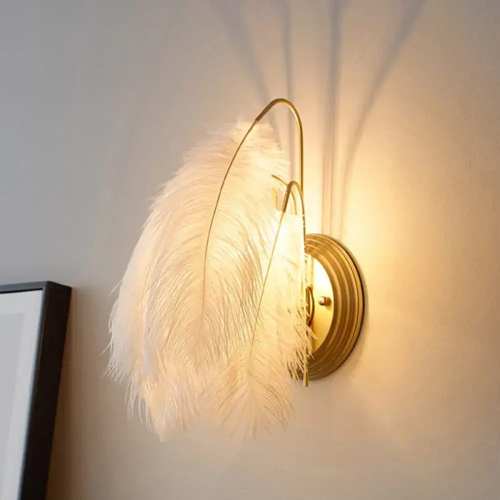 Modern grey and white furry goose feather wall lamp with delicate white feathers and gold-toned metal frame for bedroom